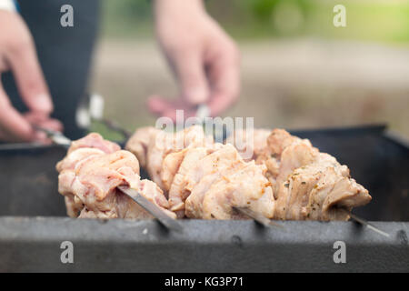 Rohes Fleisch am Spieß im Laufe der Braten. männliche Hände Schliessen gedrückt halten Spieße. Spieße mit Fleisch liegen auf einem brazier Stockfoto