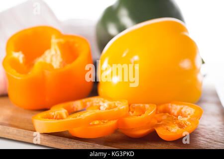 Paprika auf einem Holzbrett. Grüne und gelbe Paprika, auf eine Küche Schneidebrett. Ein Teil der Pfeffer ist mit Ringe geschnitten und liegt in der Nähe Stockfoto