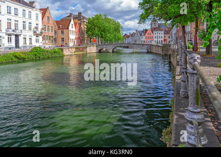 Die Canal Embankment in Brügge, Belgien. sonnigen Sommertag, Häuser auf beiden Seiten des Kanals, grünes Wasser und die Brücke in der Ferne Stockfoto