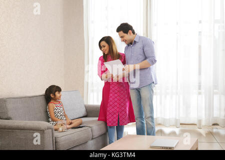 Mutter und Vater holding Papiere und Tochter sitzen auf einem Sofa mit Sparschwein Stockfoto