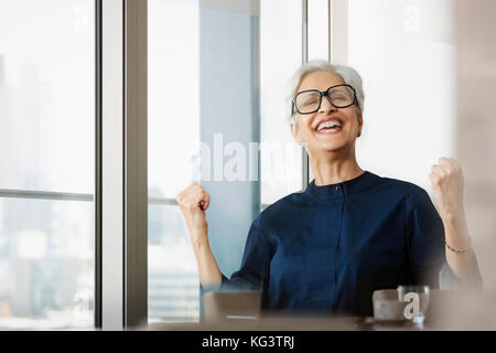 Lächelnde ältere Frau mit Brille Jubel mit Fäusten Stockfoto