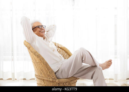 Lächelnd älterer Mann in Rattan Sessel sitzt Stockfoto