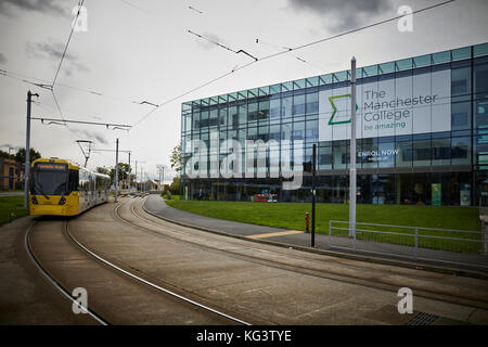 Eine gelbe Manchester Metrolink tram an Hollyhedge Straße, Benchill, Wythenshawe, Manchester College moderne geruhte Gebäude Stockfoto