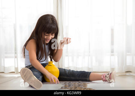 Kleines Mädchen sitzt auf dem Boden mit Lehm Sparschwein und Münzen Stockfoto