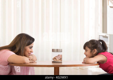 Mutter und Tochter lehnte sich auf Tabelle betrachten Geld box Stockfoto