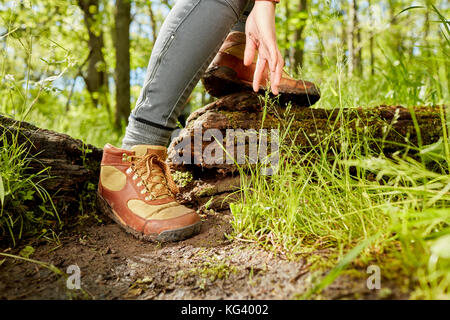 Leder Wanderschuhe und Hand eines weiblichen Wanderer in einem geringen Winkel betrachten, als sie Schritte über einen umgestürzten Baumstamm im Wald Stockfoto