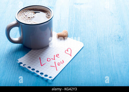 Heißer Kaffee in eine antike Schale, herzförmige Zucker und ein Stück Mathematik Papier mit den Worten lieben sie es, auf einem blauen Hintergrund im Morgenlicht. Stockfoto