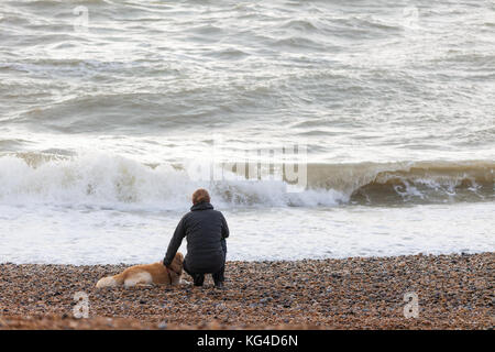 Hastings, East Sussex, UK. 4. November 2017. Rauen Bedingungen auf See in Hastings heute mit Temperaturen von 14 C und 50% Regenwahrscheinlichkeit. Mann sitzt am Strand mit seinem Hund mit Blick auf die Wellen. Foto: Paul Lawrenson/Alamy leben Nachrichten Stockfoto