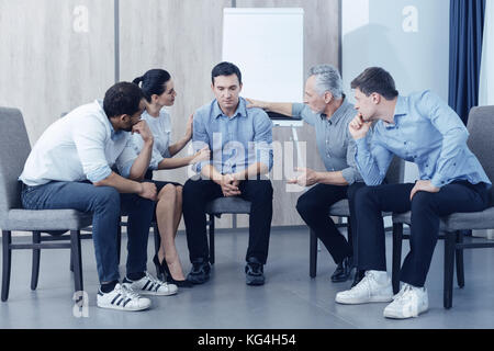 Nachdenklich männliche Person sitzt zwischen seinen Freunden Stockfoto