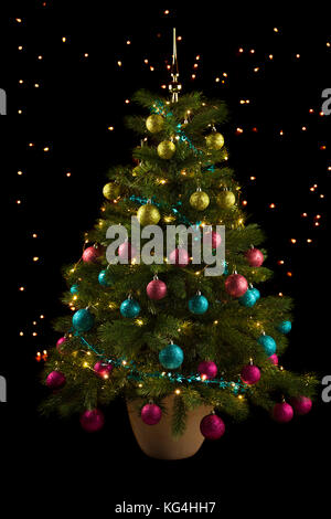 Weihnachtsbaum mit Grün, Rosa, Blau und Lila Kugeln auf schwarzem Hintergrund mit funkelnden Lichtern Stockfoto