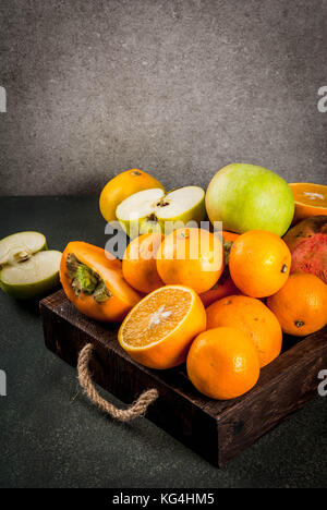 Frisches Obst Vielfalt in Holz- fach Orangen, Granatäpfel, Äpfel, Mandarinen und Persimmon. dunklen Stein Hintergrund Kopie Raum Stockfoto