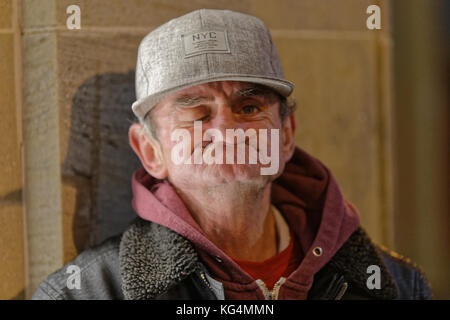 Obdachloser in Glasgow, die unterhält, Popeye Eindrücke in einem Baseball Hut gurning Stockfoto