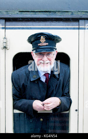 Ein Fahrkartensammler für die Dampfeisenbahn, der sich aus dem offenen Fenster einer alten Dampfeisenbahn lehnt, die in Somerset, Großbritannien, aufgenommen wurde Stockfoto