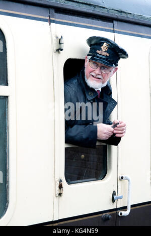 Ein Fahrkartensammler für die Dampfeisenbahn, der sich aus dem offenen Fenster einer alten Dampfeisenbahn lehnt, die in Somerset, Großbritannien, aufgenommen wurde Stockfoto