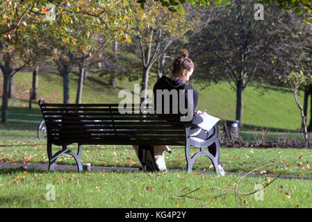 Junge Mädchen Schüler studieren in der Kelvingrove Park sonnigen Tag sitzt auf der Bank mit von hinten gesehen Stockfoto