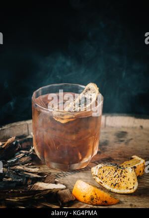 Geräucherter altmodische Cocktail garniert mit einer Orangenhaut auf dunklem Hintergrund Stockfoto