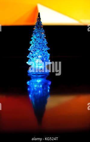 Eine kleine blaue Beleuchtung Weihnachtsbaum auf den Kontrast zu dunklen und orange geometrischen Hintergrund. selektive Fokus, Reflexionen, geometrischen Linien. abstract Col Stockfoto