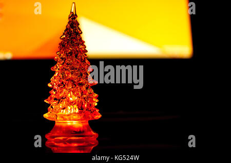 Eine kleine Beleuchtung Weihnachtsbaum auf den Kontrast zu dunklen und orange geometrischen Hintergrund. selektive Fokus, Reflexionen, geometrischen Linien. abstrakte farbenfrohe Stockfoto