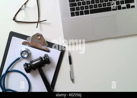 Dunkle Hammer mit medizinischen Stethoskop in der Nähe von Laptop auf weißem Schreibtisch im Gerichtssaal Konzept Stockfoto