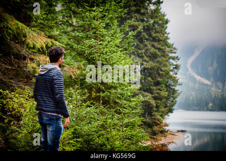 Stattliche yung Mann stand auf dem Hintergrund von Wäldern am Ufer des Sees entfernt. Stockfoto
