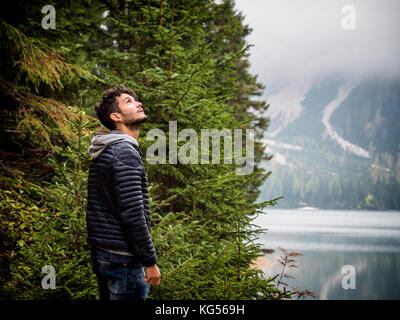 Stattliche yung Mann stand auf dem Hintergrund von Wäldern am Ufer des Sees entfernt. Stockfoto