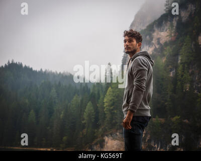 Stattliche yung Mann stand auf dem Hintergrund von Holz weg suchen. Stockfoto