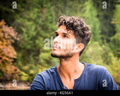 Stattliche yung Mann stand auf dem Hintergrund von Holz weg suchen. Stockfoto
