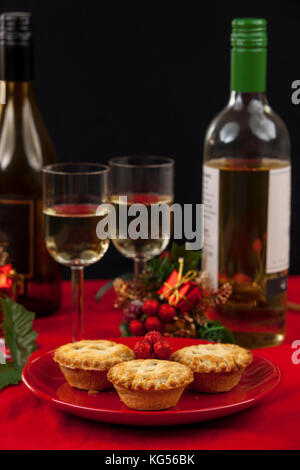 Mince Pies auf einem roten Schild mit Gläsern und Flaschen Weißwein an einem gedeckten Tisch zu Weihnachten Stockfoto