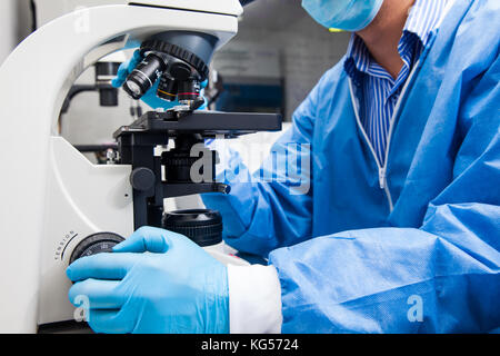 Junge männliche Wissenschaftler an Folien suchen unter dem Mikroskop Stockfoto