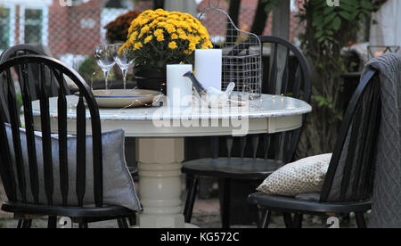 Eingerichtete runde Tisch mit Kerzen, Keramik, Weingläser, Chrysantheme Anlage mit schwarze Stühle Stockfoto