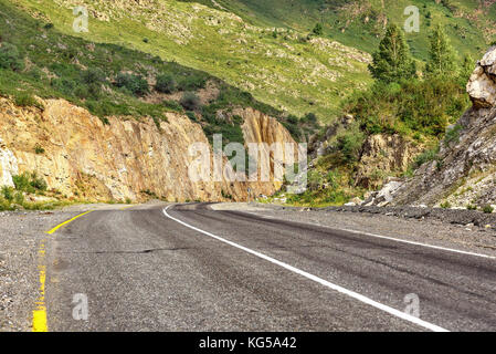 Bunter Blick auf die steilen die asphaltierte Straße in den Bergen entlang der Felsen, grünen Gras und Bäume auf der Piste Stockfoto