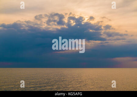 Weiche Blick auf die Sonne hinter dem regnerischen Wolken über das ruhige Meer Stockfoto