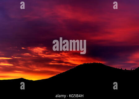 Bunte helle Sonnenaufgang in Gelb, Orange, Blau mit Wolken, die durch die Strahlen der Sonne am Himmel über den Bergen leuchtet Stockfoto