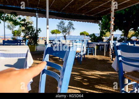 Stühle und Tische in typische griechische Taverne in der Morgensonne mit Schatten am Meeresufer. Stockfoto