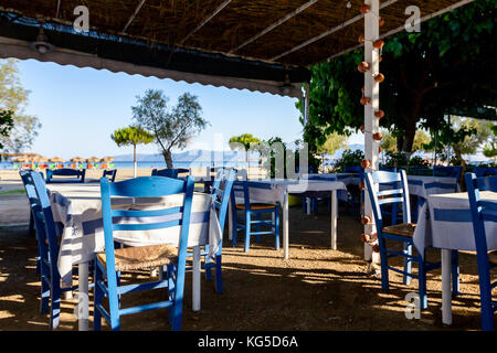 Stühle und Tische in typische griechische Taverne in der Morgensonne mit Schatten am Meeresufer. Stockfoto