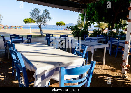 Stühle und Tische in typische griechische Taverne in der Morgensonne mit Schatten am Meeresufer. Stockfoto