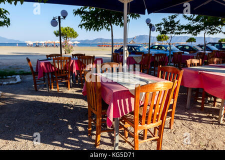 Stühle und Tische in typische griechische Taverne in der Morgensonne mit Schatten am Meeresufer. Stockfoto