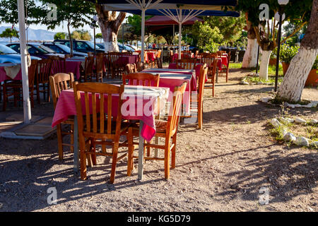 Stühle und Tische in typische griechische Taverne in der Morgensonne mit Schatten am Meeresufer. Stockfoto