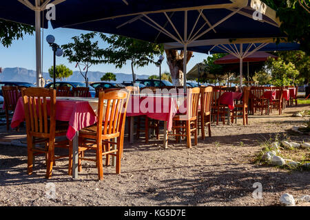 Stühle und Tische in typische griechische Taverne in der Morgensonne mit Schatten am Meeresufer. Stockfoto