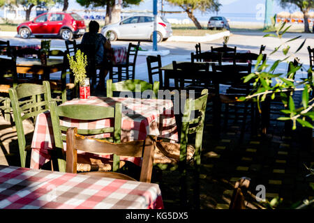 Stühle und Tische in typische griechische Taverne in der Morgensonne mit Schatten am Meeresufer. Stockfoto