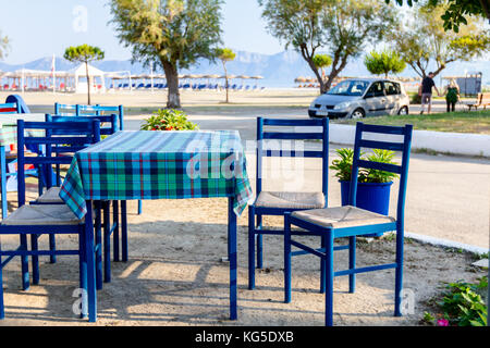 Stühle und Tische in typische griechische Taverne in der Morgensonne mit Schatten am Meeresufer. Stockfoto