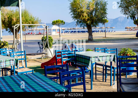 Stühle und Tische in typische griechische Taverne in der Morgensonne mit Schatten am Meeresufer. Stockfoto