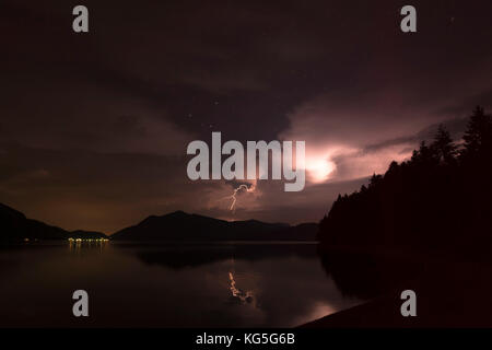 Blitzschlag am Jochberg Berg, auf der linken Seite die Lichter von urfeld (Dorf), walchensee (See walchen) vorne Stockfoto