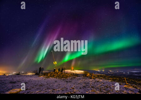 Menschen, die die Aurora Borealis oder Nordlichter auf dem Mt. Ulfarsfell, in der Nähe von Reykjavik, Island. Das Kraftwerk Hellisheidi ist in der Ferne ausgeschaltet. Stockfoto