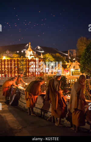 Mönche Beleuchtung Ton Kerze Schalen in der Nähe des Tempels Gebäude in Loy Krathong Festival mit vielen Feuer Laterne auf den Nachthimmel. Chiang Mai, Thailand. Stockfoto