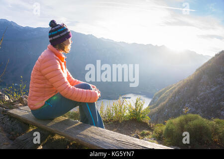 Junge Frau sitzt auf dem Zweig auf dem Aussichtspunkt, Entspannung nach Wandern und Beobachten die Bohinj See, Slowenien Stockfoto