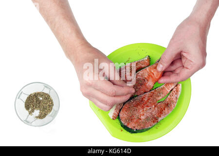 Die Hände der alten Opa Koch sprengte Gewürze und Kräuter auf frischen Lachs Fisch Steaks. auf weißem Top View Studio isolierte Schuß Stockfoto