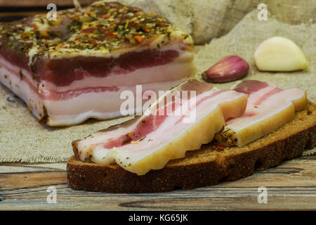 Es ist ein großes Stück gesalzener Speck auf dem Tisch. zwei Scheiben Speck liegen auf einer Scheibe Brot Stockfoto