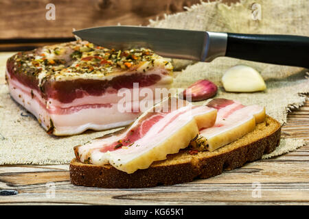 Auf dem Tisch ist eine Scheibe brot mit zwei Scheiben frisch gesalzen Rost, ein großes Stück Speck und Knoblauchzehen Stockfoto