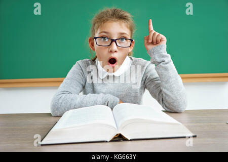 Wussten Sie, dass?! Neugierige Schülerin liest ein Buch. Foto der erstaunt kleines Mädchen Brille zeigenden Finger. Bildung Konzept Stockfoto